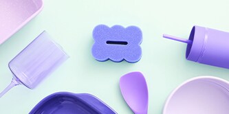 Estropajo morado Brite de Scotch-Brite™ expuesto con utensilios de cocina en tonos pastel sobre la encimera.
